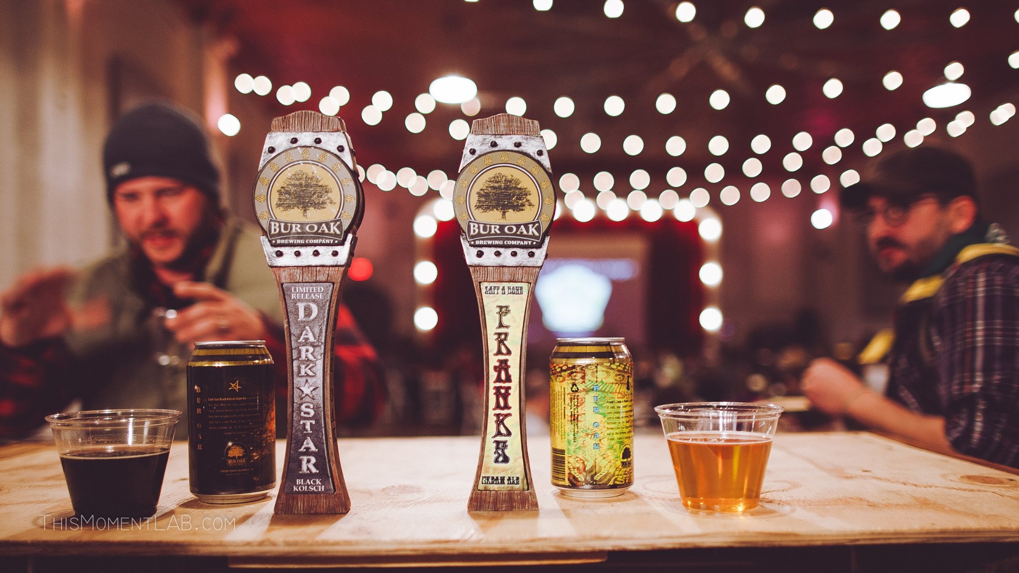 countertop with cups and cans of dark and light beer with 2 men in the background