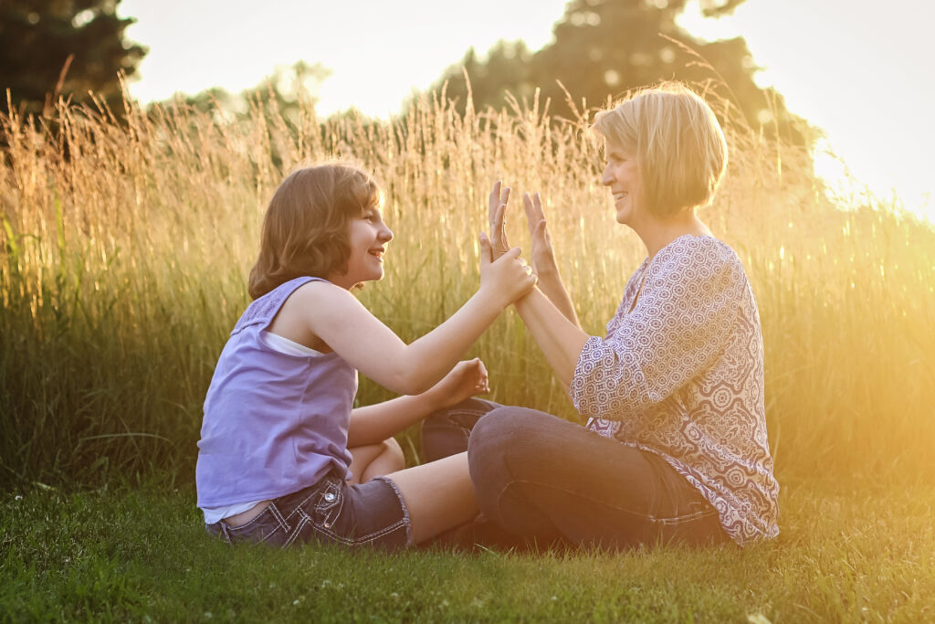A woman sitting with a young girl on the autism spectrum in a grassy field.