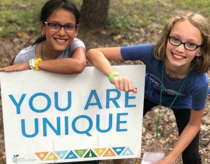 Two young girls at Camp Encourage next to a sign that reads "You are unique"